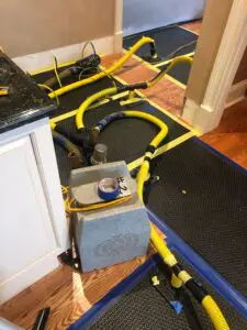 A kitchen floor with pipes and wires laying on it.