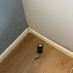 A cell phone sitting on the floor of a corner room.