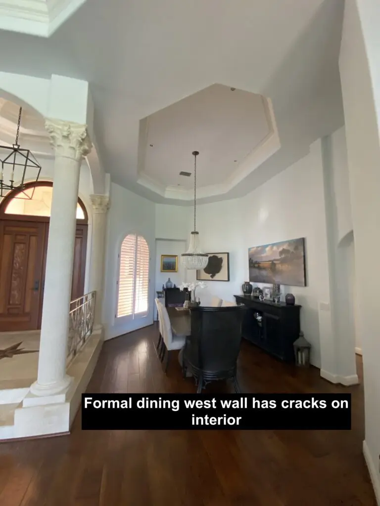 A formal dining room with a large wall has cracks on the ceiling.